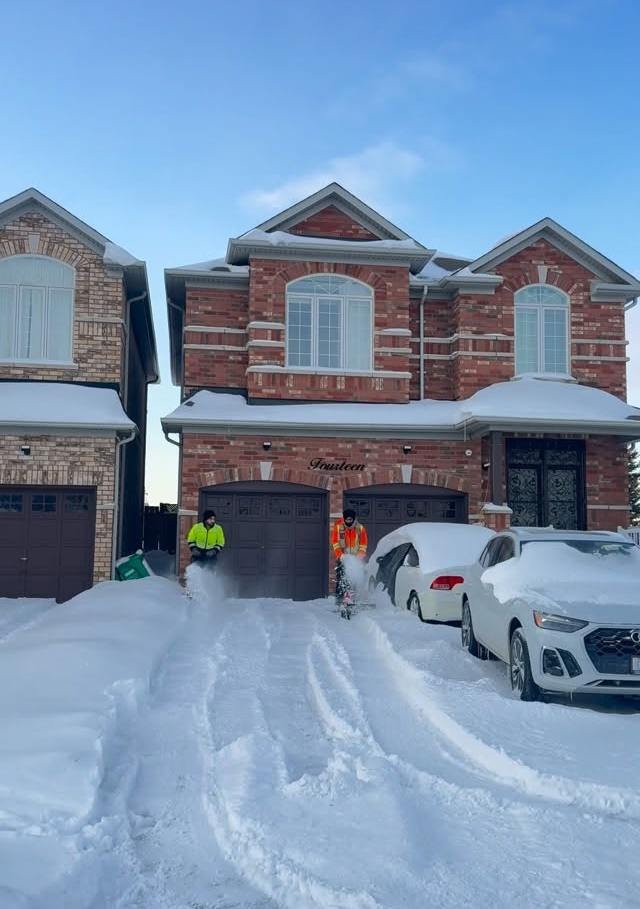 GRD crew clearing a snowy double driveway in front of a brick house