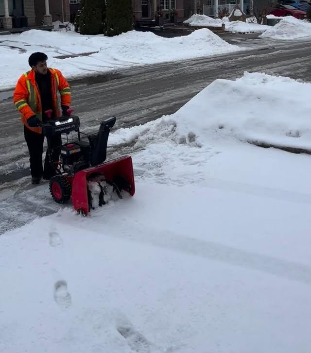 GRD worker in a safety vest running a snowblower along a street